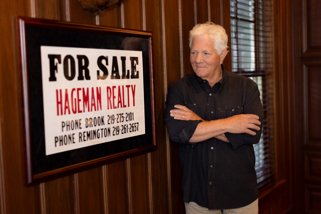 Steve Hageman beside a framed early Hageman Realty For Sale sign listing phone numbers in Brook and Remington