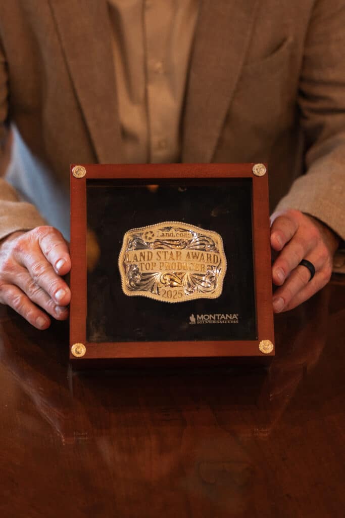 A 2025 Land.com Land Star Award Top Producer belt buckle in a wooden display case